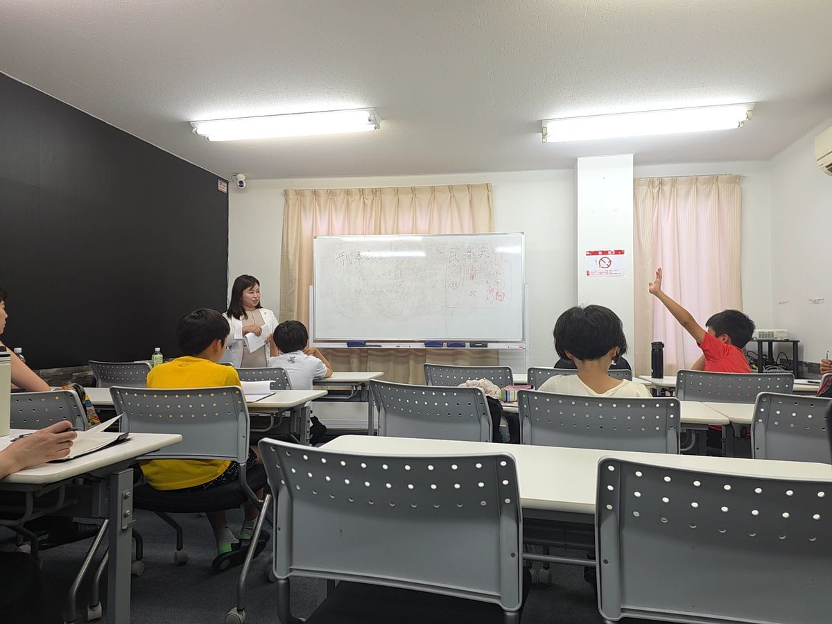 明るい教室で生徒が手を挙げて発言しようとしている授業風景