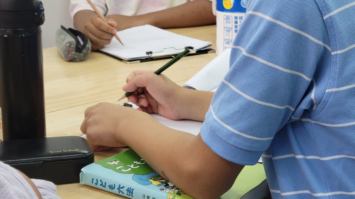 『こども六法』を傍らにノートへ書き込む生徒の手元