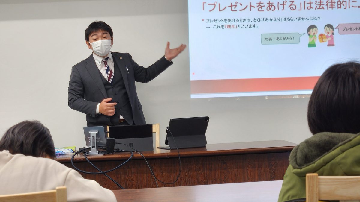 スライドを使って説明する講師と、机に向かう生徒たちの教室の様子